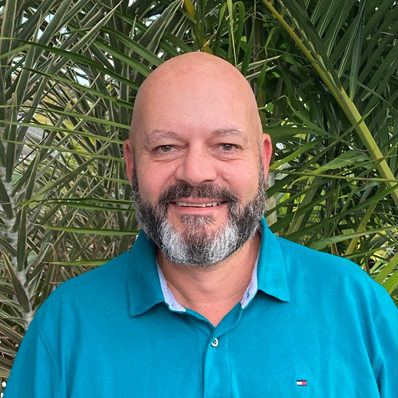 Director of Regional Development, Anthony Shreenan headshot in a blue shirt with palm leaves behind